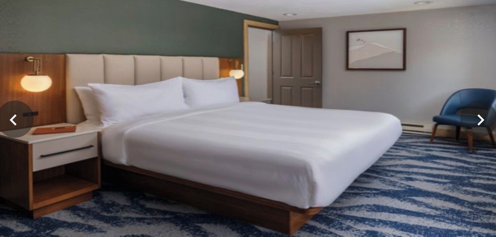 A hotel room with a large bed, a nightstand, a chair, and a door.