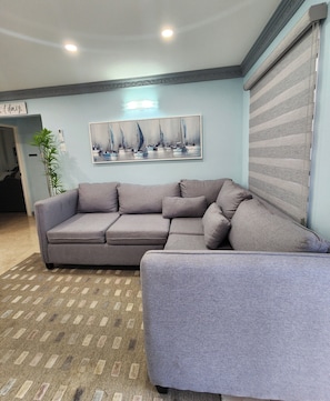 A living room with a sectional sofa, a painting of sailboats, a striped blind, and a patterned rug. - Elegant 2-bedroom retreat in Montego Bay (Montego Bay)