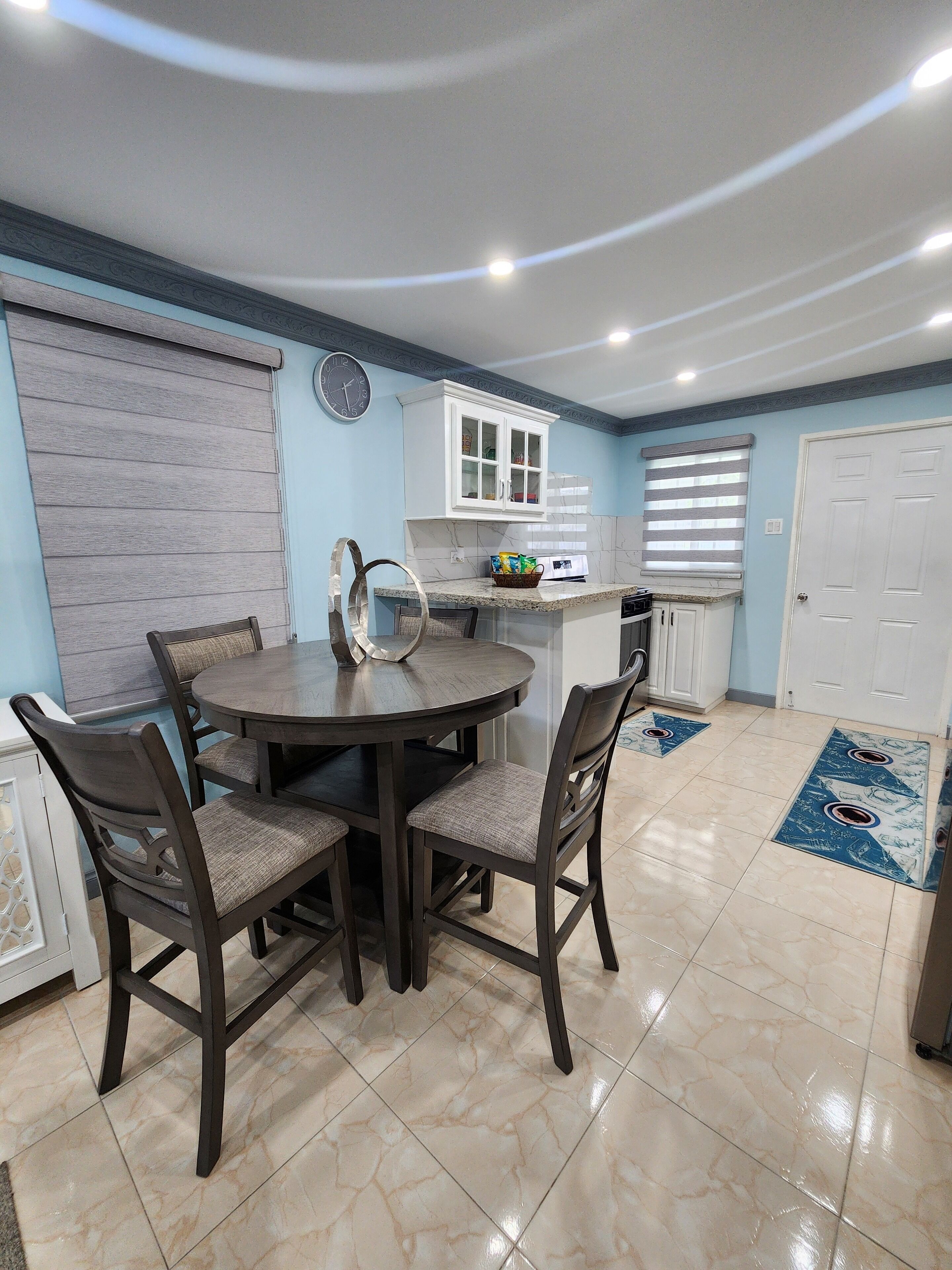 A dining area with a round table and four chairs, a kitchen with white cabinets, a microwave, and a refrigerator.
