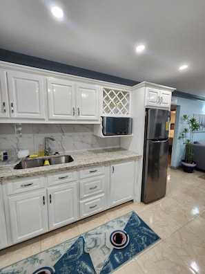 A modern kitchen with white cabinets, a stainless steel refrigerator, a microwave, and a sink. - Elegant 2-bedroom retreat in Montego Bay (Montego Bay)