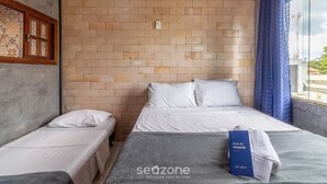 Quarto de hotel com duas camas, uma parede de tijolos, uma janela com cortinas e uma placa na cama.