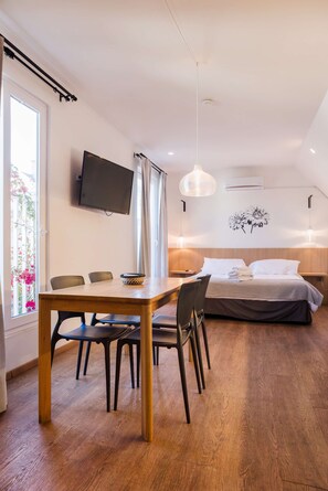 A bedroom with a bed, bedside tables, a TV, and a dining area with chairs and a table. - Providencia: Modern Studio with Balcony & Metro! (Providencia)