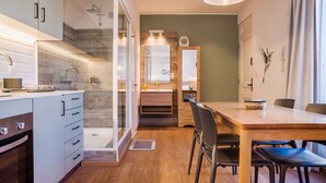 Una cocina moderna con horno empotrado, un comedor con mesa y sillas de madera y una zona de ducha con puerta de cristal.