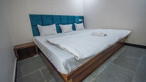 A single bed with a wooden frame and a blue headboard, white bedding, and a small wooden bench at the foot of the bed. - Hotel Vishwas Lok (Ujjain)