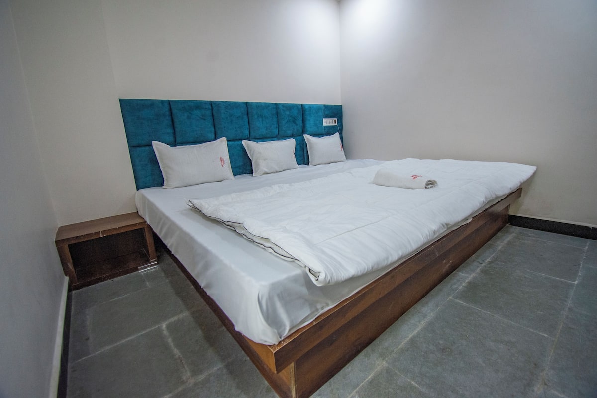 A single bed with a wooden frame and a blue headboard, white bedding, and a small wooden bench at the foot of the bed.