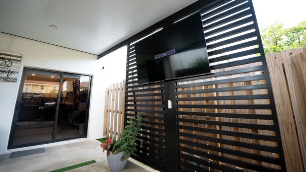 A modern outdoor patio area with a sliding glass door leading to a kitchen, a black metal fence, and a potted plant. - Cozy Princeton Getaway (Homestead)