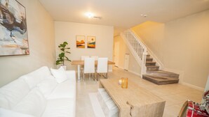 A modern living room with a white sofa, a wooden coffee table, and a staircase leading to another level. - Cozy Princeton Getaway (Homestead)