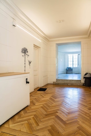 A spacious room with wooden parquet flooring, a white radiator, and a door leading to another room.