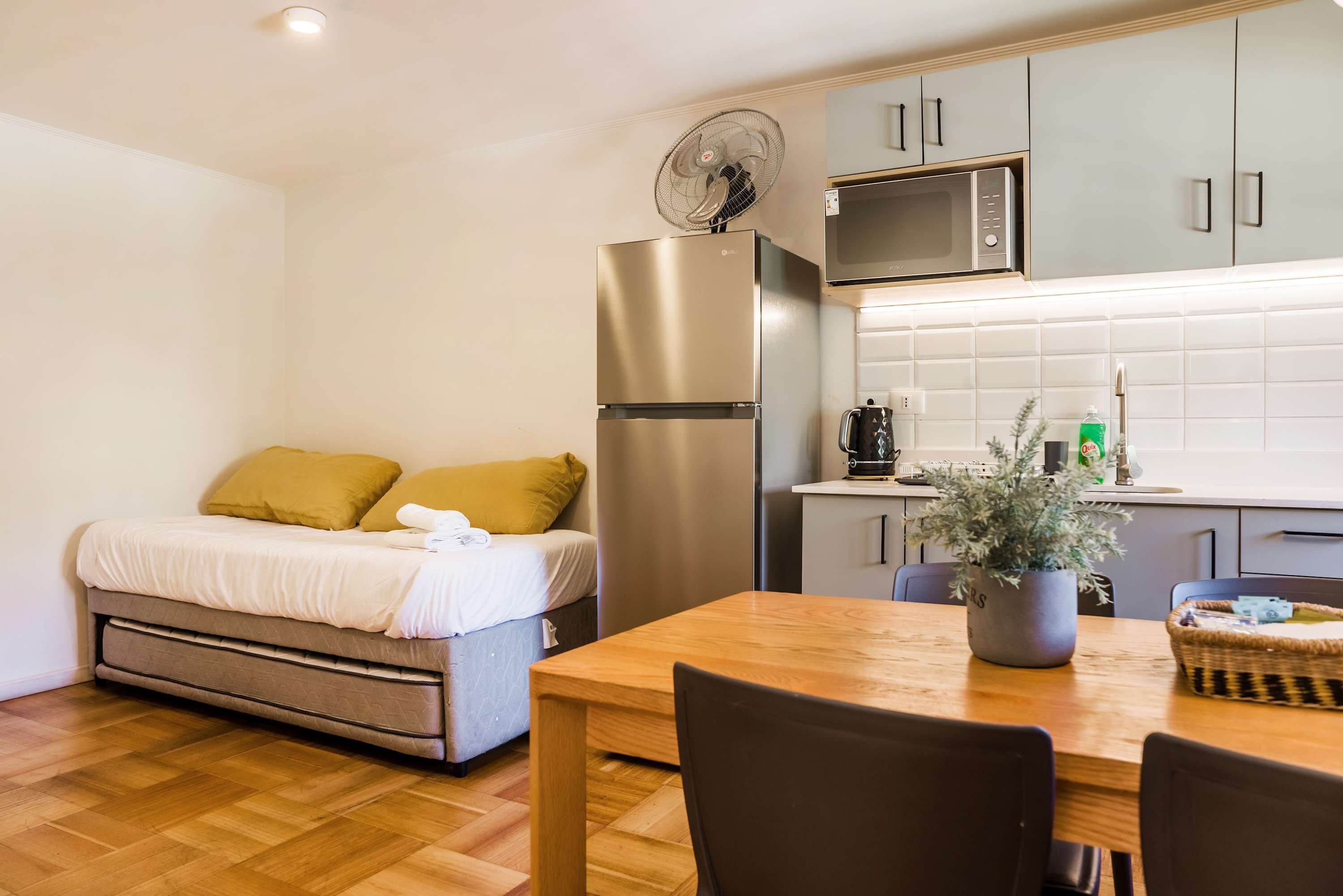 A compact room with a bed, a dining table, a refrigerator, a microwave, and a small kitchen area.