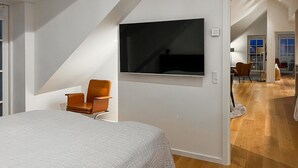 Ett modernt sovrum med en säng, en TV som är monterad på väggen och en stol.