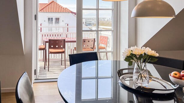 En matplats med ett bord, stolar, en vas med blommor och en skål med frukt.