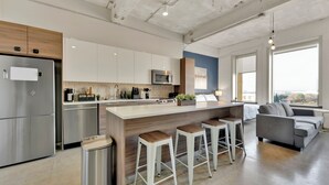 A modern kitchen with a central island, bar stools, and a grey sofa in a living area with a view. - Luxury 1BR Apt I King Beds I Free Parking I Gym (Dallas)