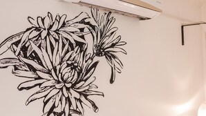 Een muur met een zwarte bloemensticker, een aan het plafond gemonteerde airconditioner, en een wandpaneel van houten latten.