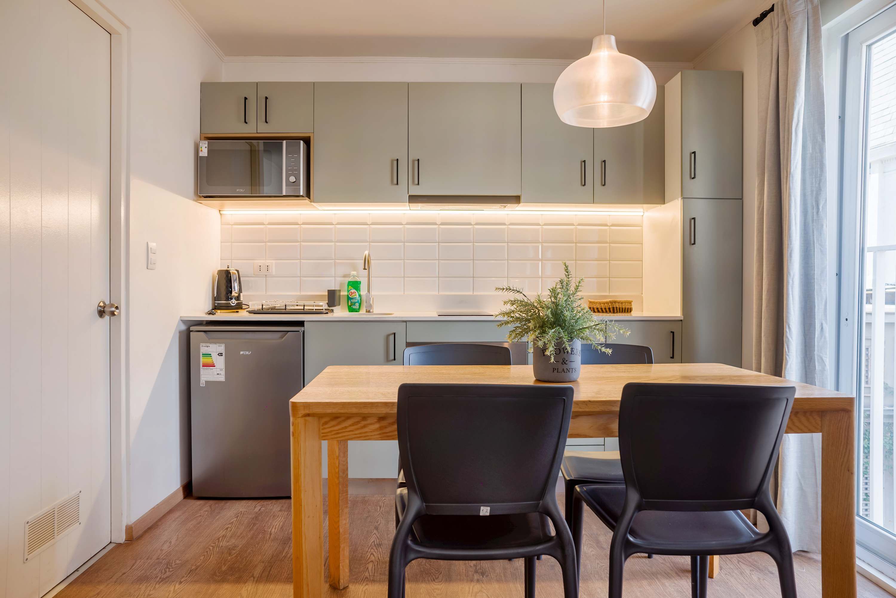 Une cuisine moderne avec des meubles gris, un four à micro-ondes, un réfrigérateur et une table à manger avec des chaises.