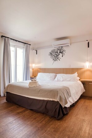 Ein ordentlich bezogenes Bett mit brauner Bettdecke, eine Wandklimaanlage und ein Wandbild.