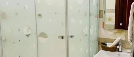 Casa de banho com cabine de duche em vidro, lavatório e espelho.