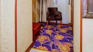 Un pasillo estrecho con alfombra estampada, una silla, una lámpara y una escalera.