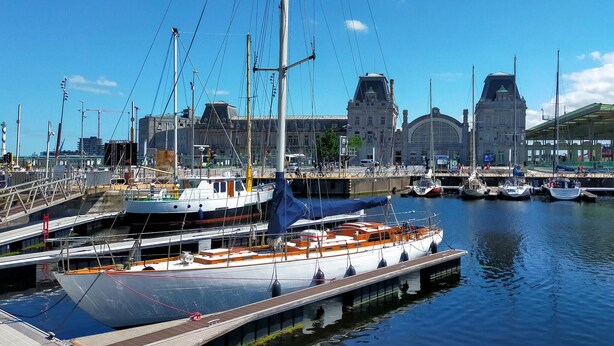 A marina with multiple boats docked, a large building with a clock tower in the background, and a pedestrian bridge over the water. - Amazing apartment in Oostende with WiFi (Oostende)