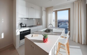 Ett modernt kök med vita skåp, en inbyggd ugn och en stor köksö med en växt.