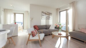 A modern living room with a grey sofa, a white armchair, a glass coffee table, and a dining area with a white table and chairs. - Amazing apartment in Oostende with WiFi (Oostende)