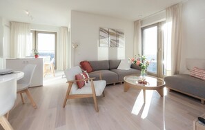 Ett modernt vardagsrum med en grå soffa, en vit fåtölj, ett glasbord och en matplats med ett vitt bord och stolar.