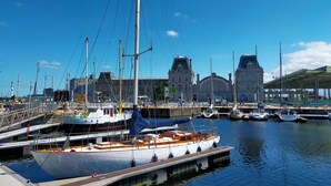 Puerto deportivo con barcos amarrados, un edificio grande con torre de reloj y una zona cubierta con tejado verde.