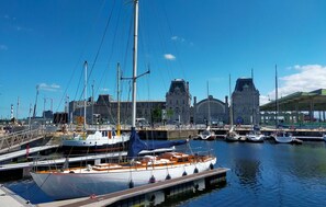Ein Yachthafen mit vertäuten Booten, ein großes Gebäude mit einem Uhrturm und ein überdachter Bereich mit einer Gründachfläche.