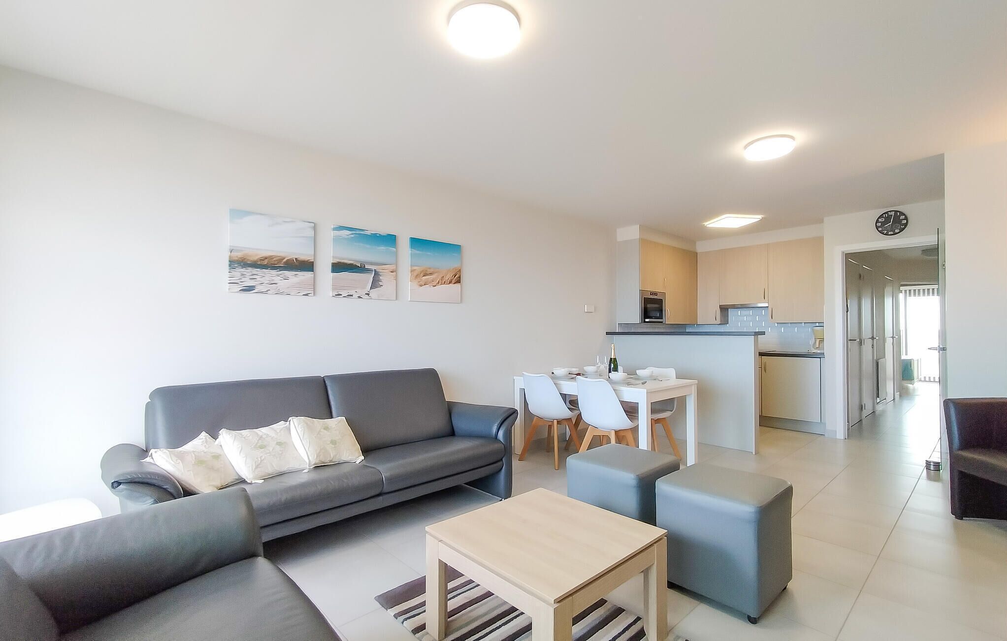 Een moderne woonkamer met een grijze bank, een houten salontafel en een eethoek met witte stoelen en een kleine tafel.
