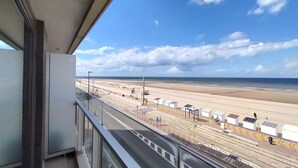 Vista desde un balcón sobre una playa, una vía de tren y un cielo despejado.
