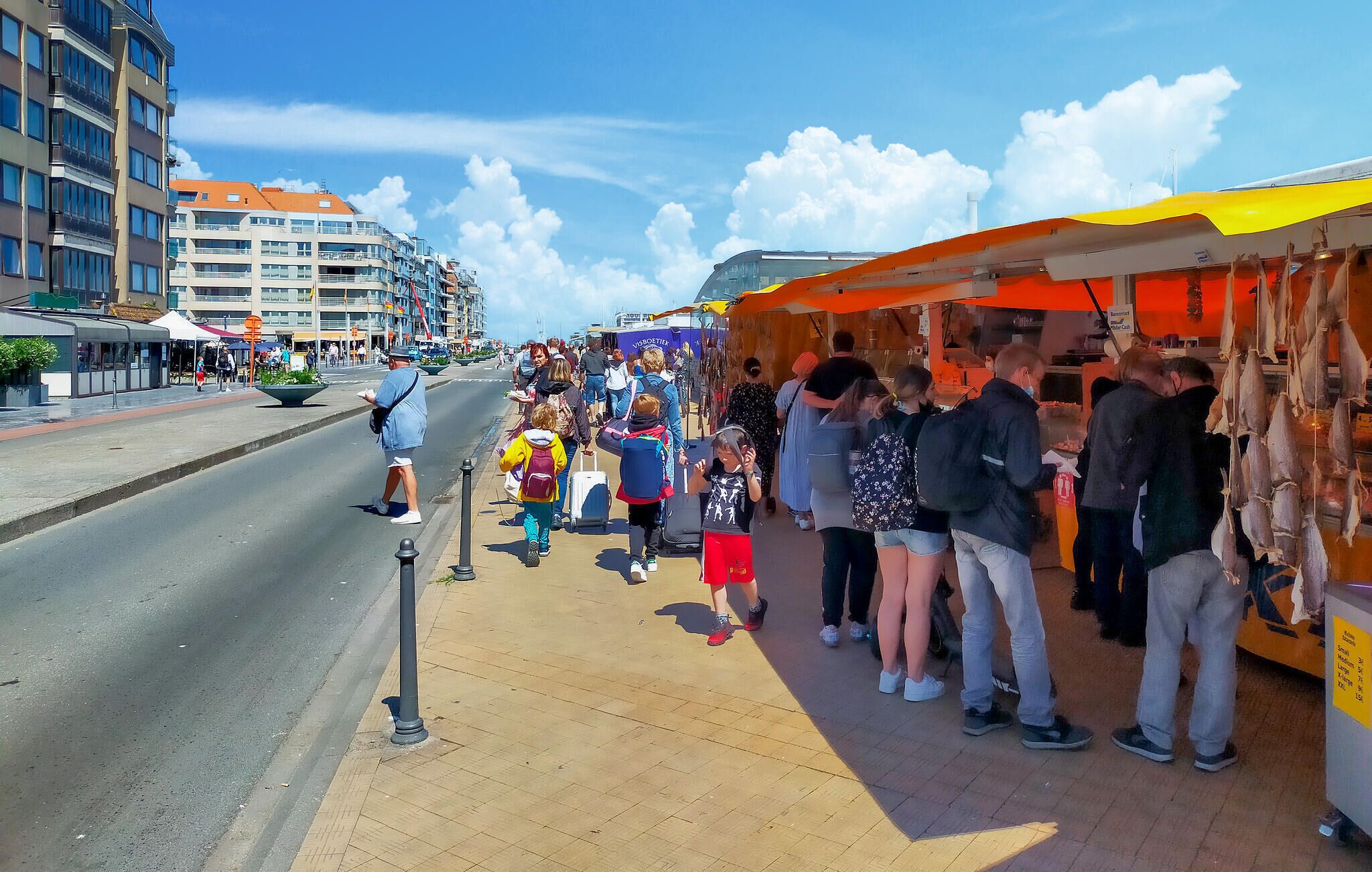 Une rue animée, avec des passants et un étal de nourriture installé sur le trottoir.