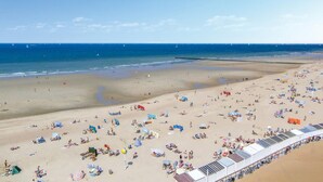 Ein Strand mit vielen Liegestühlen und Sonnenschirmen, ein sandiger Uferstreifen und ein klarer, blauer Himmel.