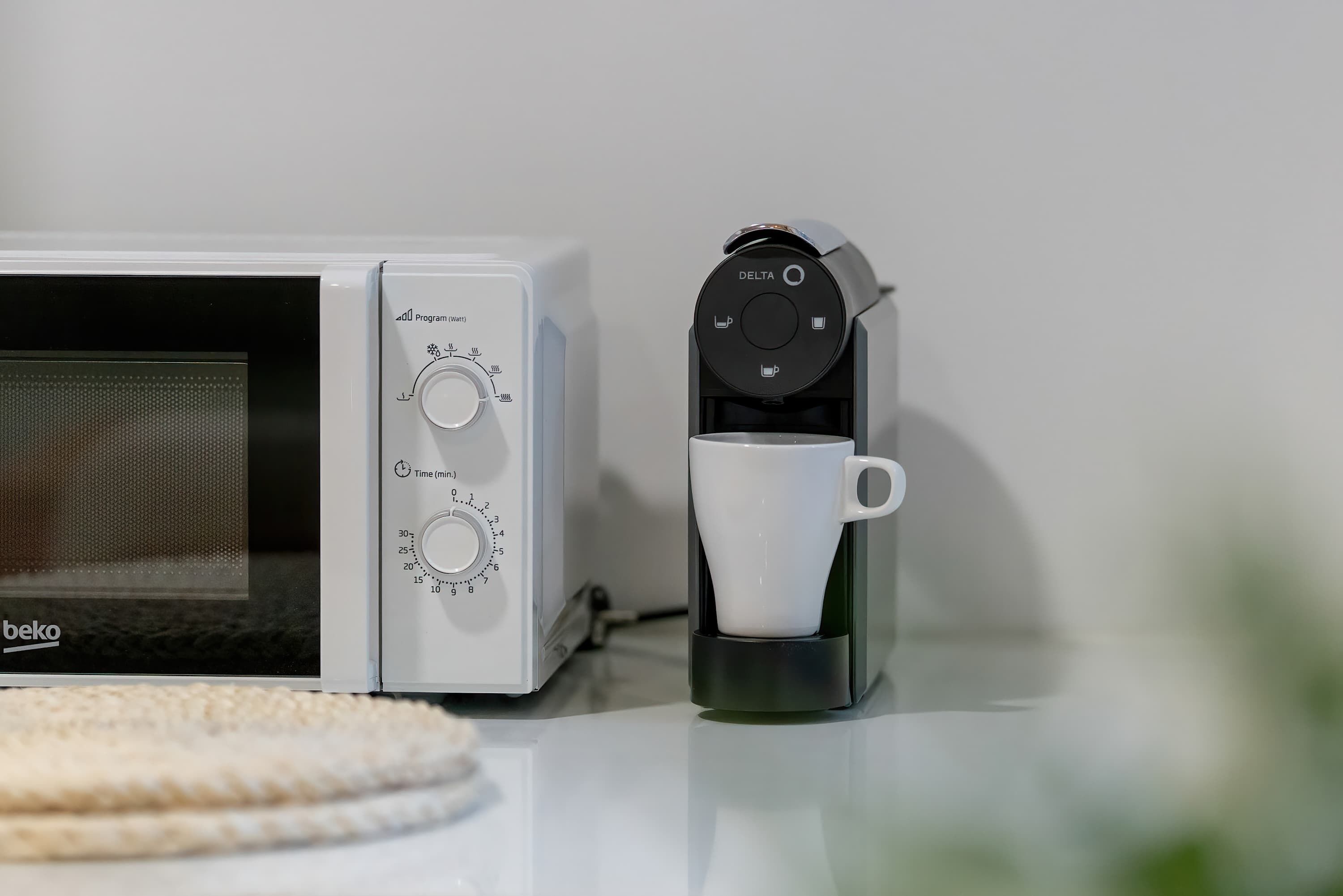 A microwave and a coffee maker with a cup on the counter.