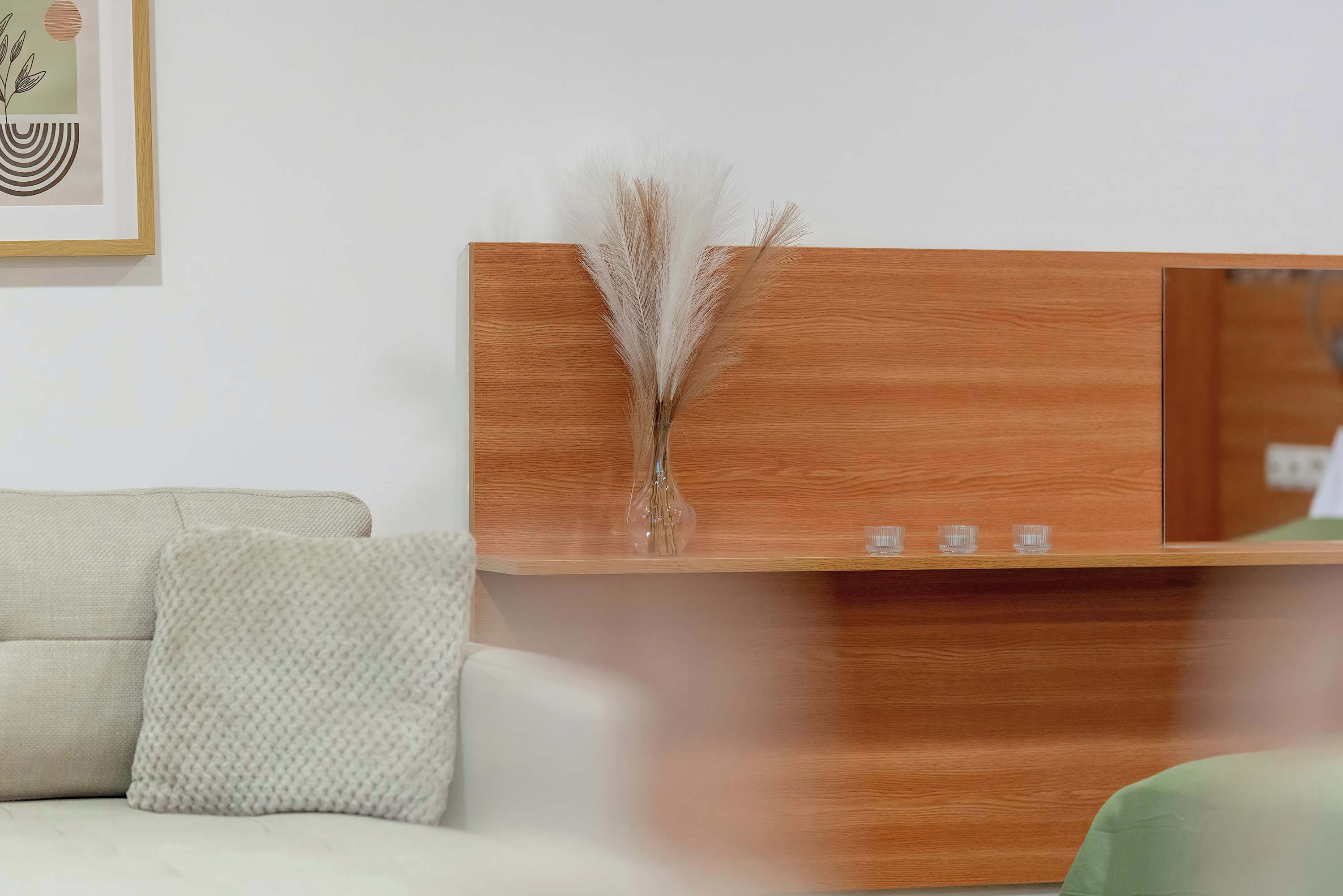 Un comptoir d’accueil moderne avec un revêtement en bois, un vase contenant des herbes des pampas séchées et une œuvre d’art encadrée accrochée au mur.