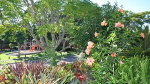 Un jardín exuberante con diversas plantas y un parque infantil al fondo.