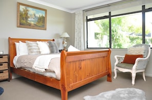 Une chambre à coucher avec un lit en bois, une chaise, une lampe et une fenêtre donnant sur des arbres.