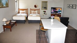 Habitación de hotel con dos camas, un comedor con mesa y sillas, un televisor y una mesita de noche con lámpara.
