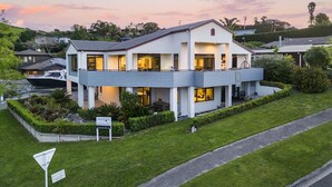 Una casa moderna de dos pisos con balcón, rodeada de céspedes cuidados y un muelle para embarcaciones.