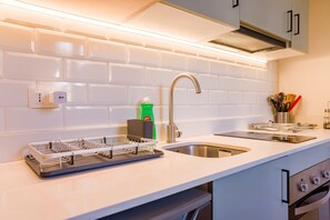 A modern kitchen with white subway tiles, stainless steel appliances, and a dish rack. - Chic Studio in Salvador Sleeps 4 Near Metro (Providencia)