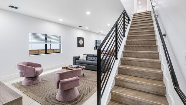 A modern living room with a staircase, a sofa, two armchairs, and a coffee table.