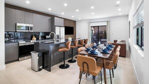 A modern kitchen with a central island, bar stools, and a dining area with a table set for four. - Group getaway w/ soccer suites & hot tubs (Miami)