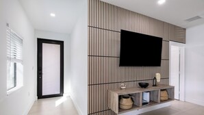 Un pasillo moderno con panel de madera, televisor montado y una consola con cestas.