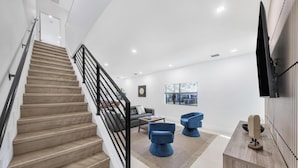 Una sala de estar moderna con una escalera, un televisor de pantalla plana montado en la pared y un ventanal grande.