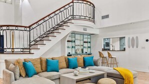 Una sala de estar moderna con una escalera curva, un sofá modular, una mesa de centro y un comedor con sillas.