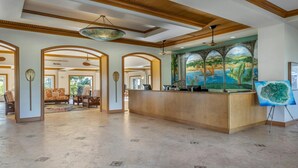 Un vestíbulo amplio con una mesa de recepción, arcos y un mural grande que muestra un paisaje tropical.