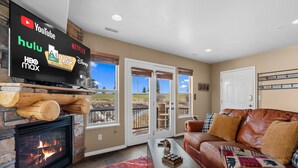 A living room with a fireplace, a leather couch, a coffee table, and a TV displaying streaming services. - Hidden Moose Lodge MH610 | Near Snowbasin|Eden, Ut (Eden)