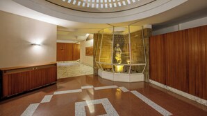 Un vestíbulo con un recinto de vidrio que exhibe una estatua, un panel de pared de madera y un piso estampado.