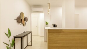 Un área de recepción con un mostrador de madera, una planta en maceta y un ventilador de pared.