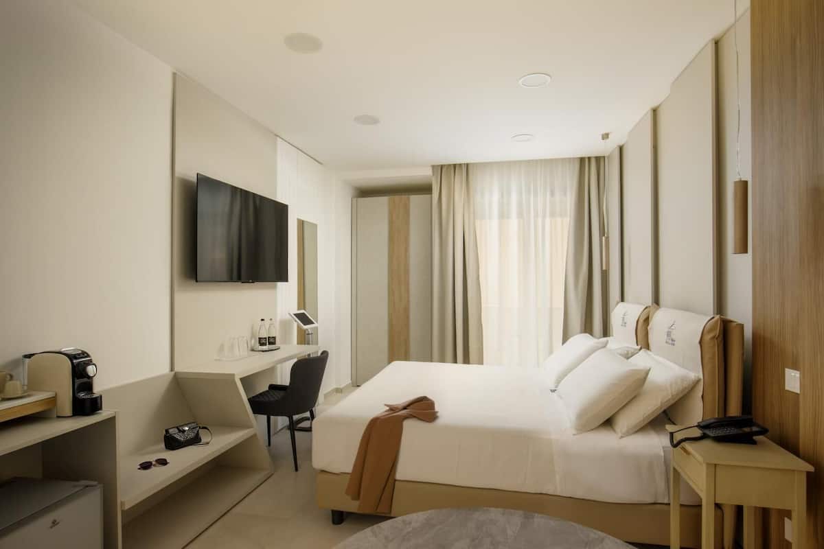 A hotel room with a bed, a desk, a chair, a TV, and a window with curtains.