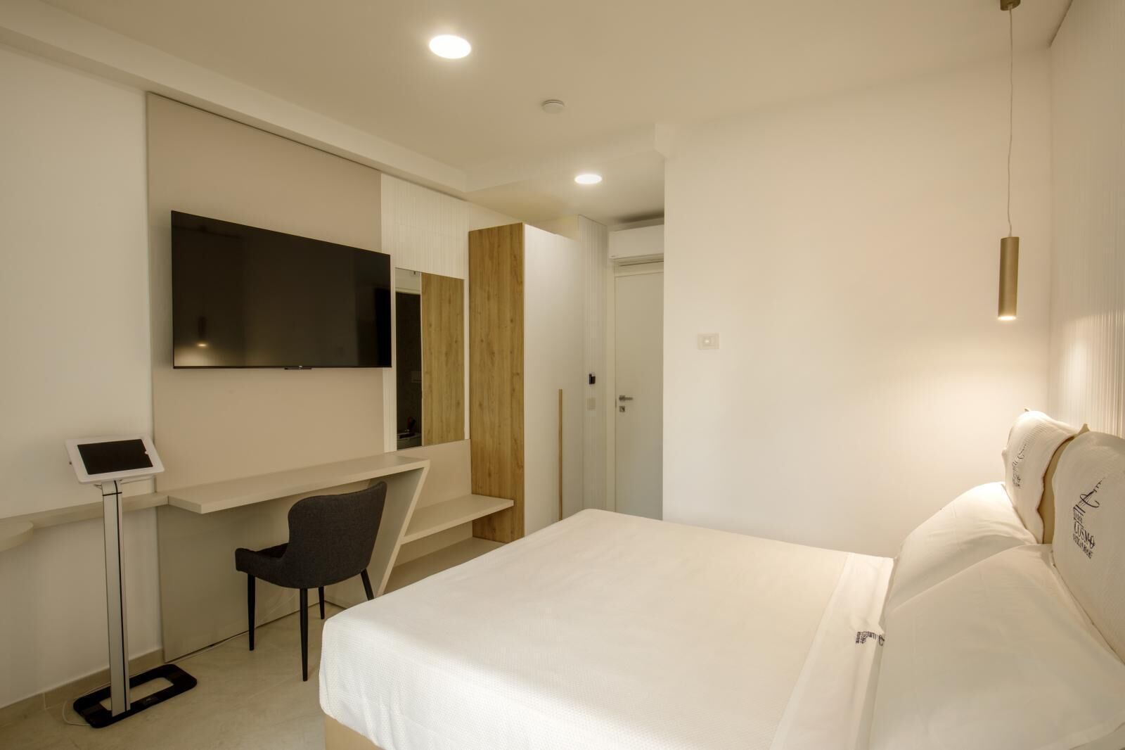 Una habitación de hotel moderna con una cama, un escritorio con silla, un televisor montado en la pared y una mesita de noche.