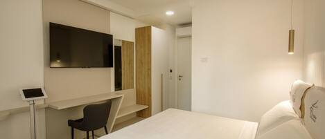 Una habitación de hotel moderna con una cama, un escritorio con silla, un televisor montado en la pared y una mesita de noche.